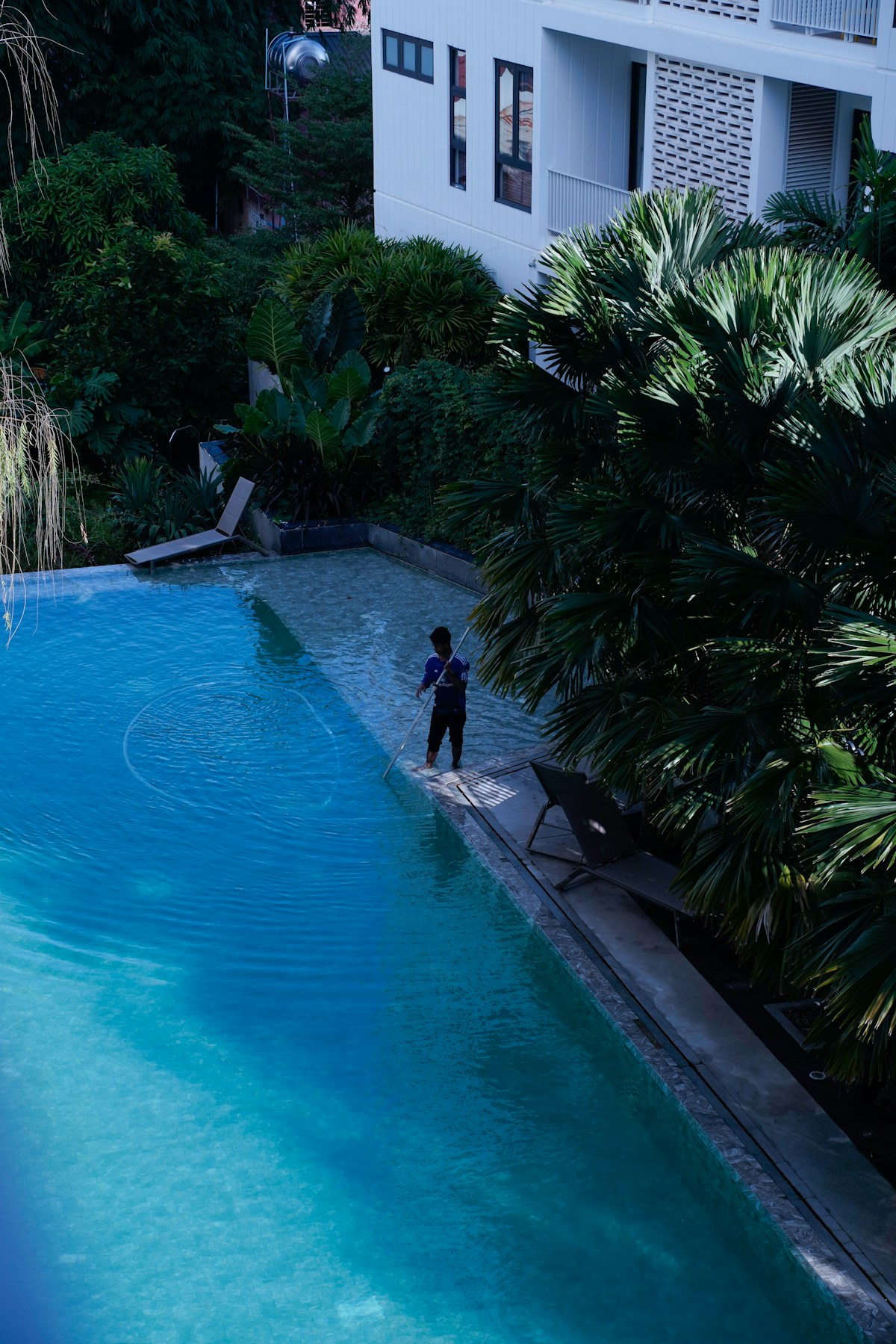 Hospitality property maintenance employee cleaning a resort pool.